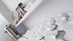 Una cocina con gabinetes blancos, una cafetera y una hilera de tazas y platitos blancos.