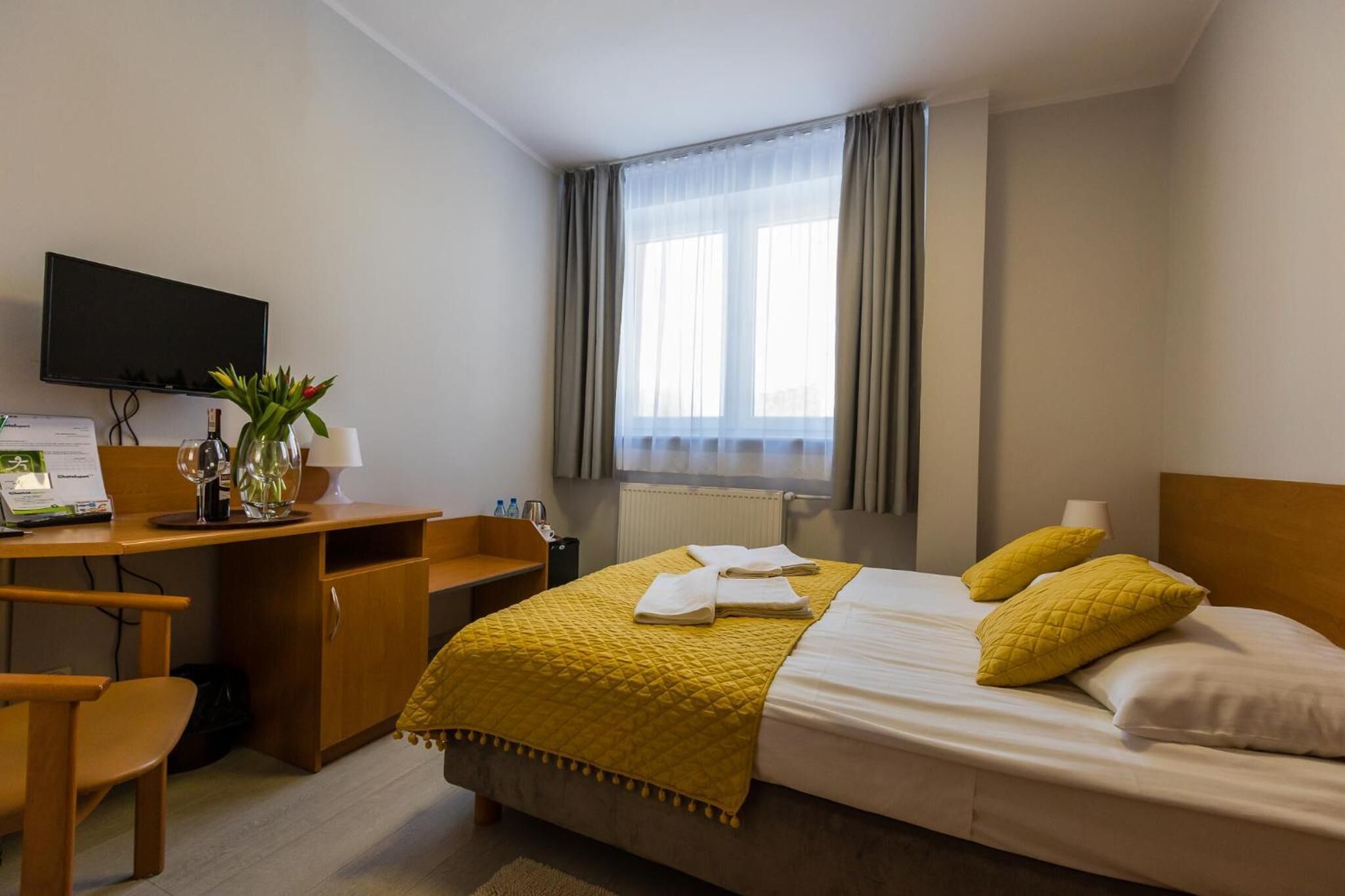 Habitación de hotel con cama, escritorio, silla, televisión y ventana con cortinas.