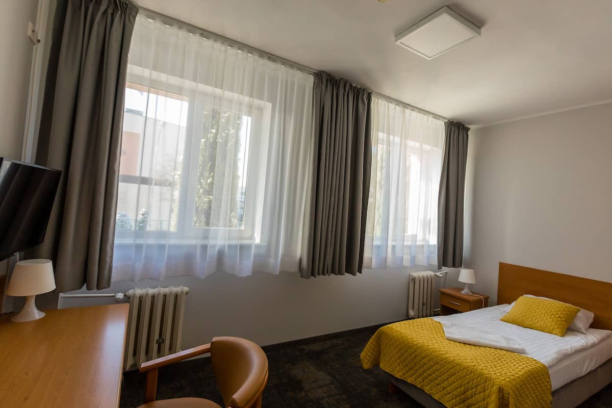 A hotel room with a bed, a desk with a chair, a TV, and a window with curtains.