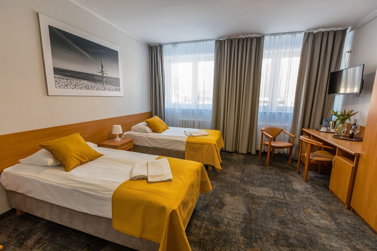 A hotel room with two beds, a desk, a chair, a TV, and a painting on the wall.