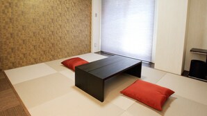Een kamer met tatami vloerbedekking, een lage tafel en twee rode kussens.