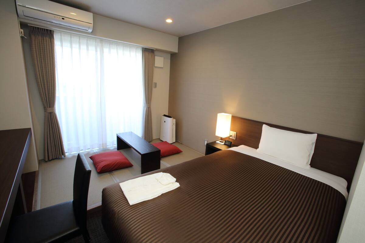 A hotel room with a large bed, a desk, a chair, a lamp, and a window with curtains.