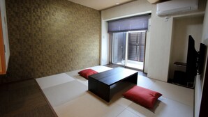 Een kamer met tatami vloerbedekking, een lage tafel en twee rode kussens.