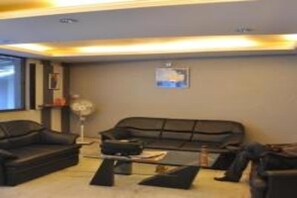 A living room with a black sofa, a coffee table, and a fan. - Hotel Rajdhani Plaza (Ranchi)