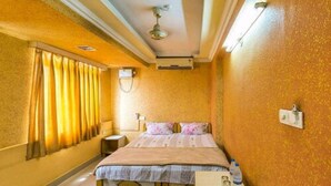 Habitación de hotel con cama, cortinas, ventilador de techo, equipo de aire acondicionado y mesita de noche con una botella.