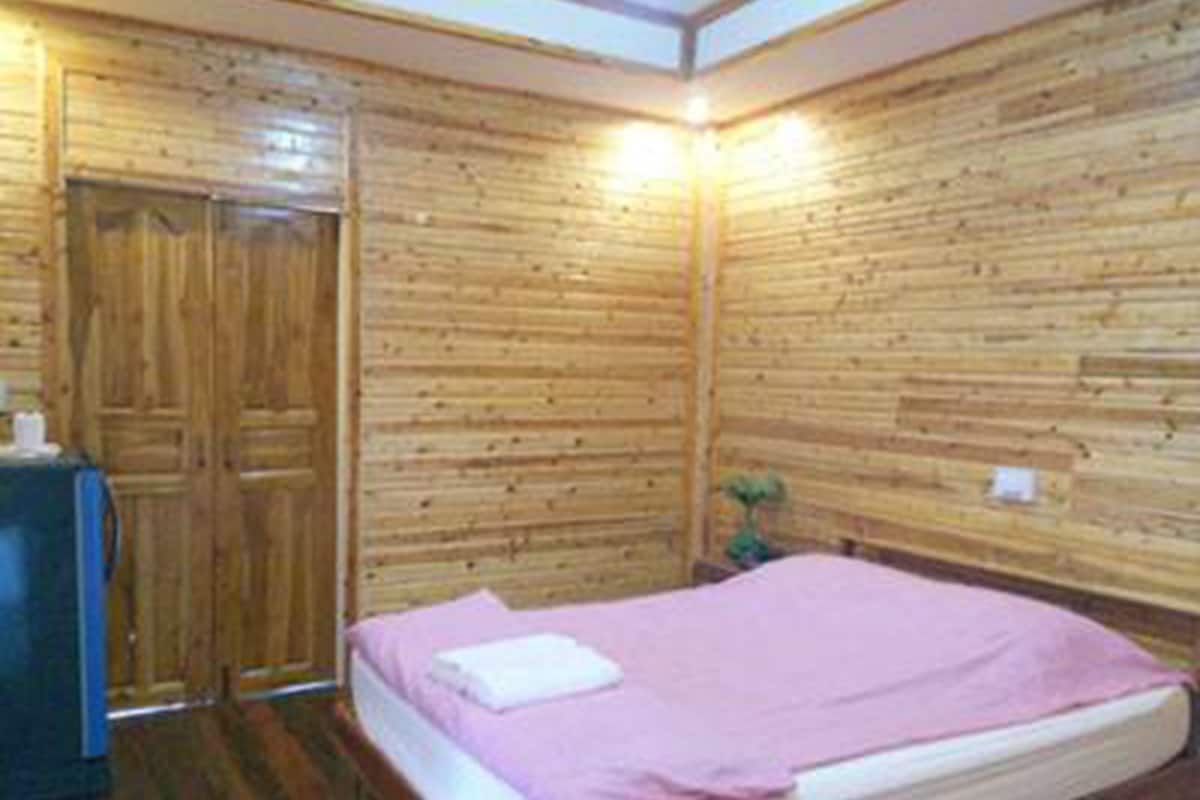 Una habitación con paredes de madera, una cama con una colcha rosa y una pequeña mesa con un objeto blanco encima.
