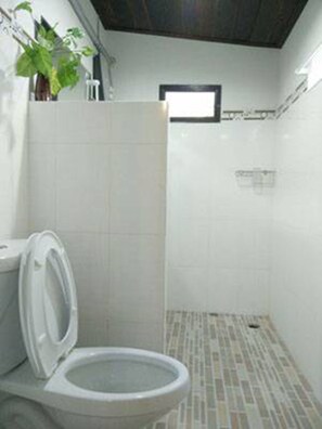 A bathroom with a toilet, a shower area, and a small window.