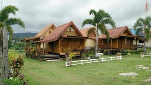 Ein Haus aus Holz mit einem Strohdach, umgeben von einem weißen Zaun und Palmen.