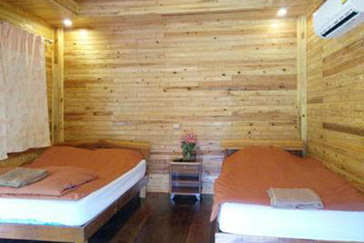 Una habitación tipo cabaña de madera con dos camas, una mesita pequeña y un equipo de aire acondicionado.