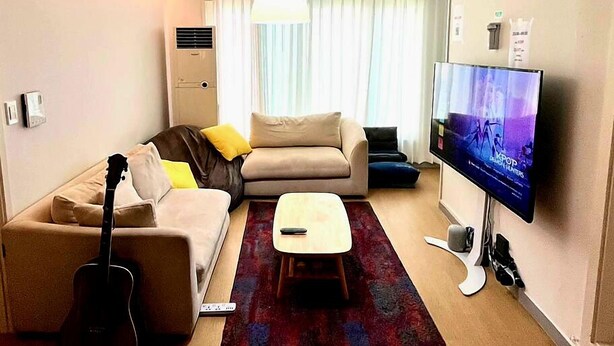 Una sala de estar con un sofá, una mesa de centro, un televisor, una guitarra y una alfombra roja.