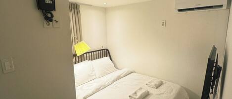 Habitación de hotel con cama, escritorio, silla, televisión de pantalla plana y aire acondicionado instalado en el techo.