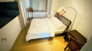 Habitación de hotel con cama, lámpara de noche, mesita de noche de madera, perchero y aire acondicionado de pared.
