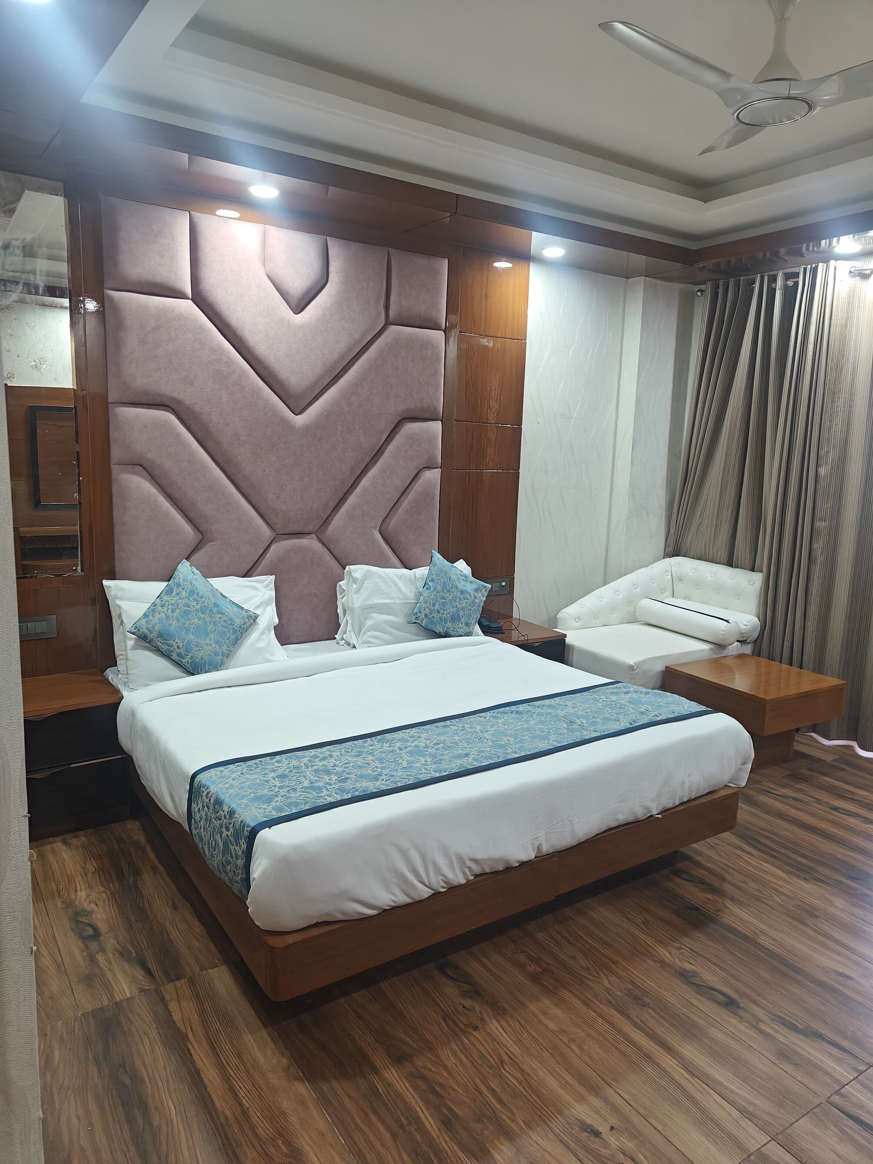 A modern bedroom with a large bed, a bedside table, a nightstand, a ceiling fan, and a window with curtains.