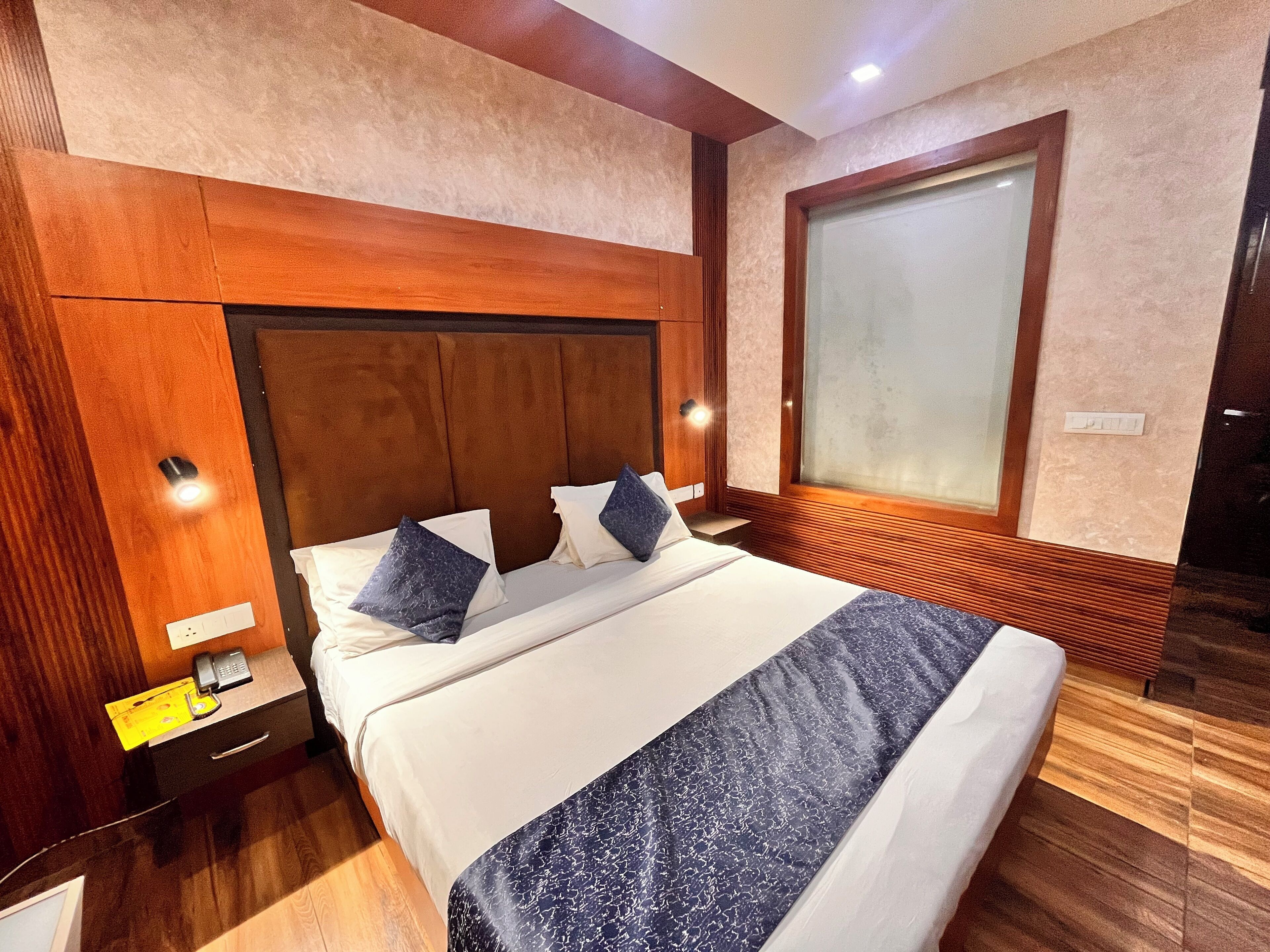 A hotel room with a large bed, wooden headboard, bedside tables, and a large window with frosted glass.