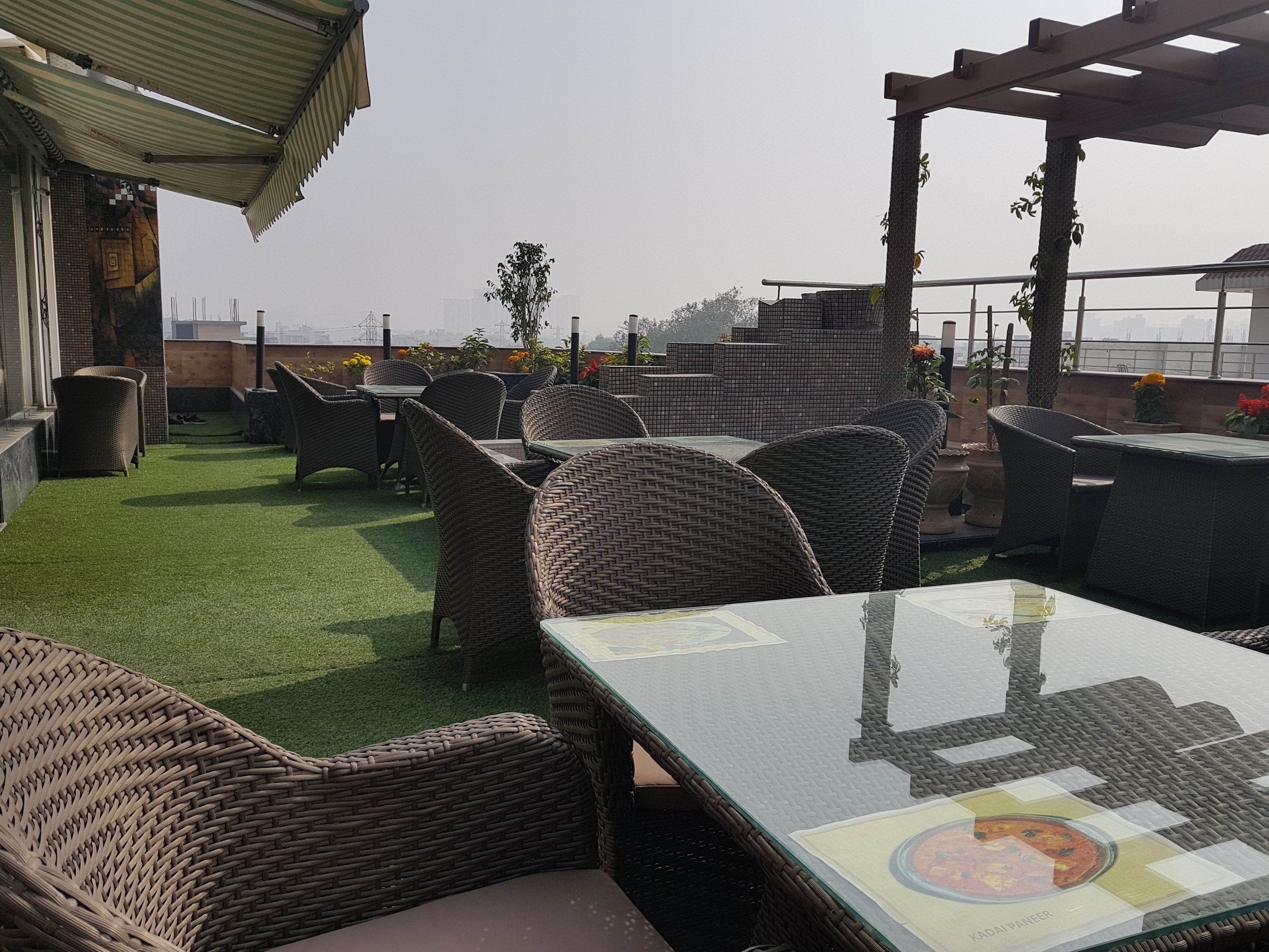 Een terras met rieten meubels en een glazen tafel, omgeven door kunstgras en potplanten.