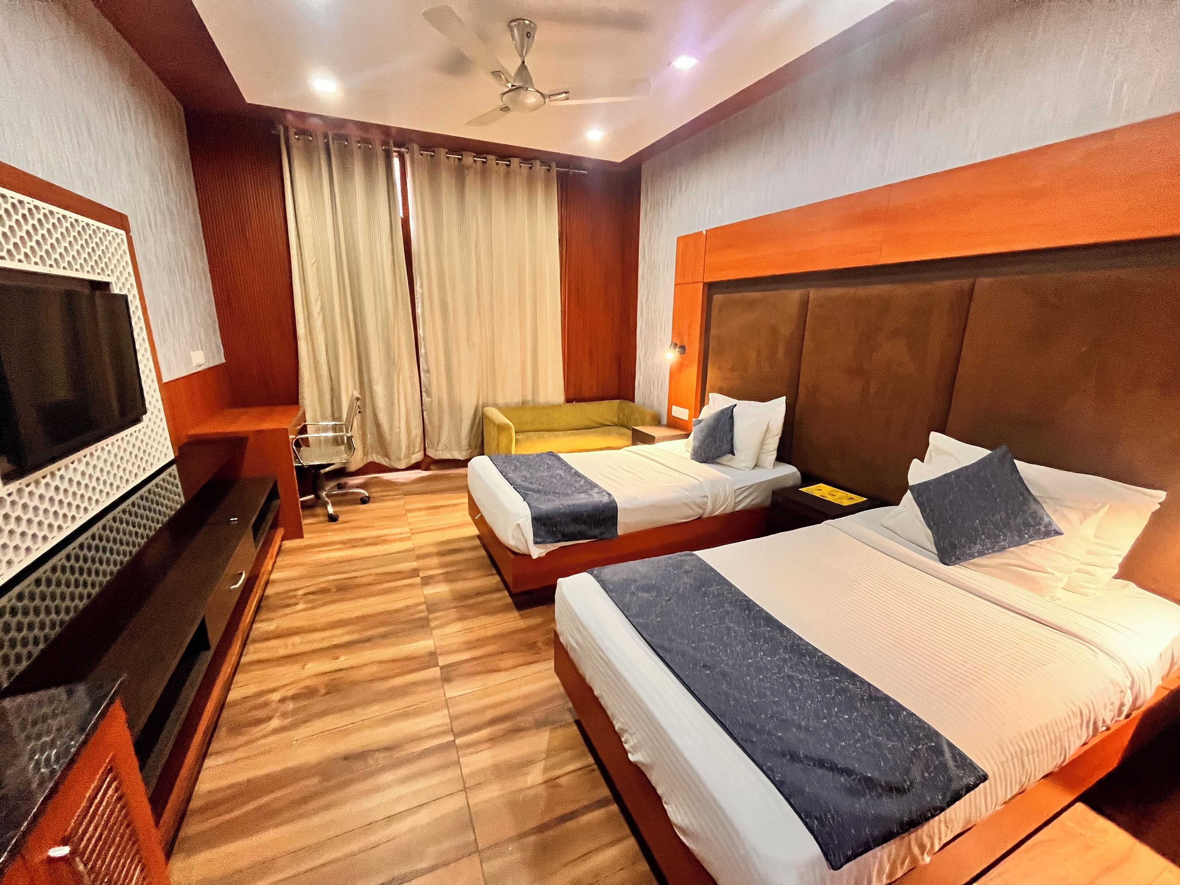 A hotel room with two beds, a TV, a desk, and a ceiling fan.