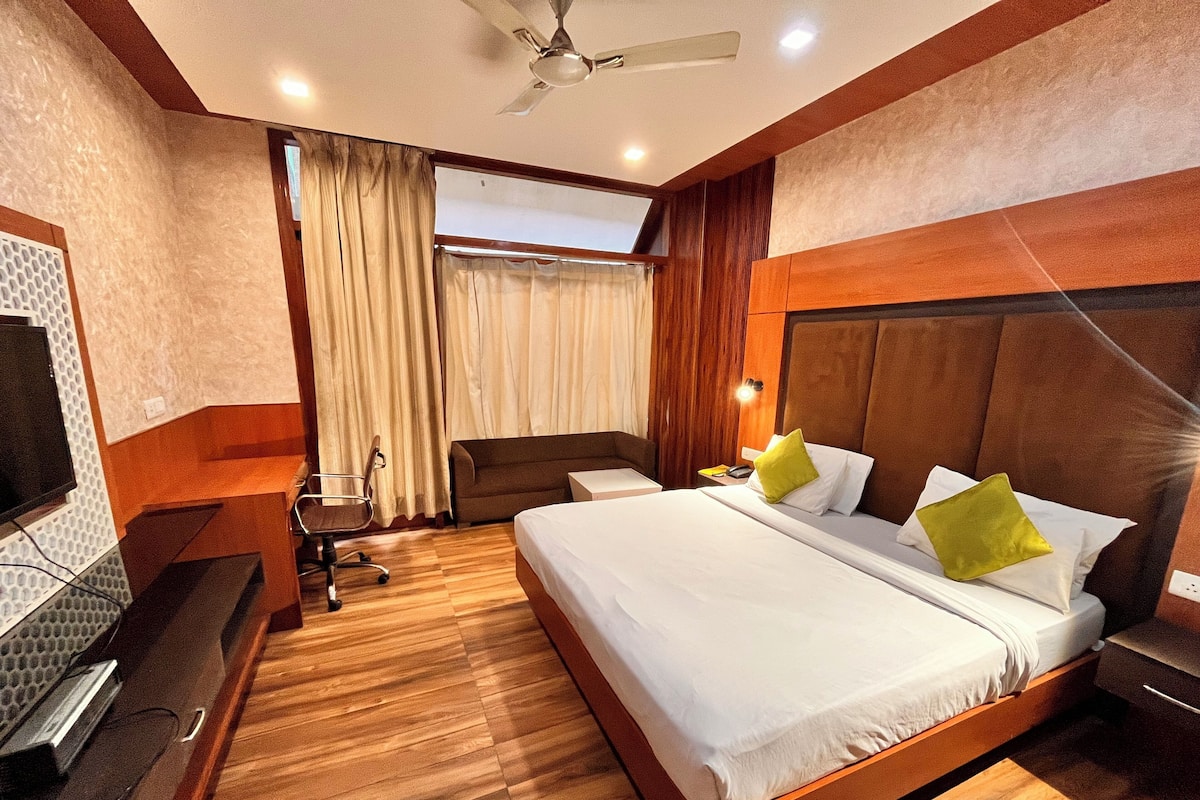 A hotel room with a large bed, a desk, a chair, and a television.