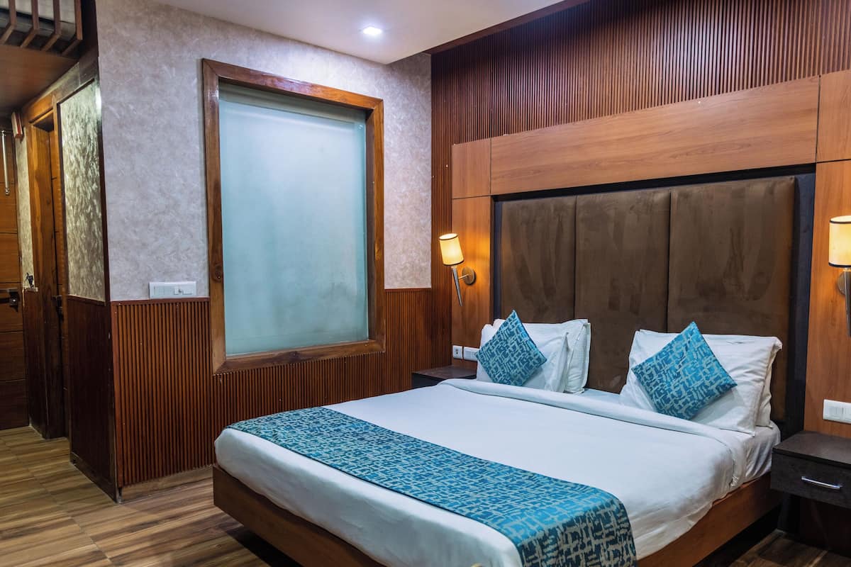 A hotel room with a large bed, wooden headboard, two bedside tables with lamps, a large window with frosted glass, and a wooden floor.