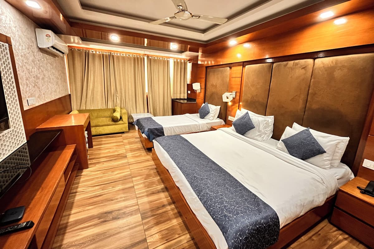 A hotel room with two beds, a sofa, a TV, and a ceiling fan.