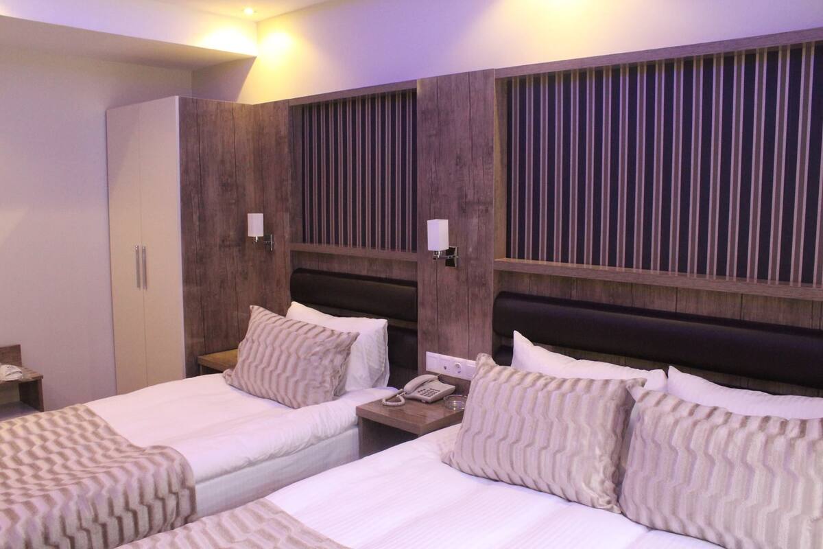 Una habitación de hotel con dos camas, un armario, mesitas de noche con lámparas y un teléfono.