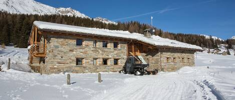 A stone building with a wooden balcony, a ski lift, and a snow-covered mountain in the background.