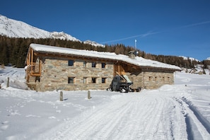 A stone building with a wooden balcony, a ski lift, and a snow-covered mountain in the background.