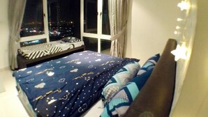 Quarto com uma janela grande, uma cama com roupa de cama estampada e cortinas.