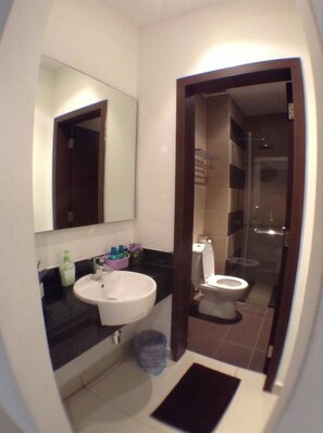 A compact bathroom with a white sink, a mirror, a toilet, and a shower area. - HomeStay in Johor - KSL Fun House (Johor Bahru)