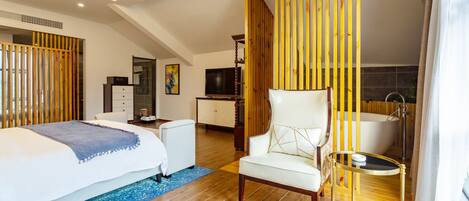 Une chambre d’hôtel moderne dotée d’un grand lit, d’un coin salon, d’une télévision, d’un bureau et d’une baignoire.
