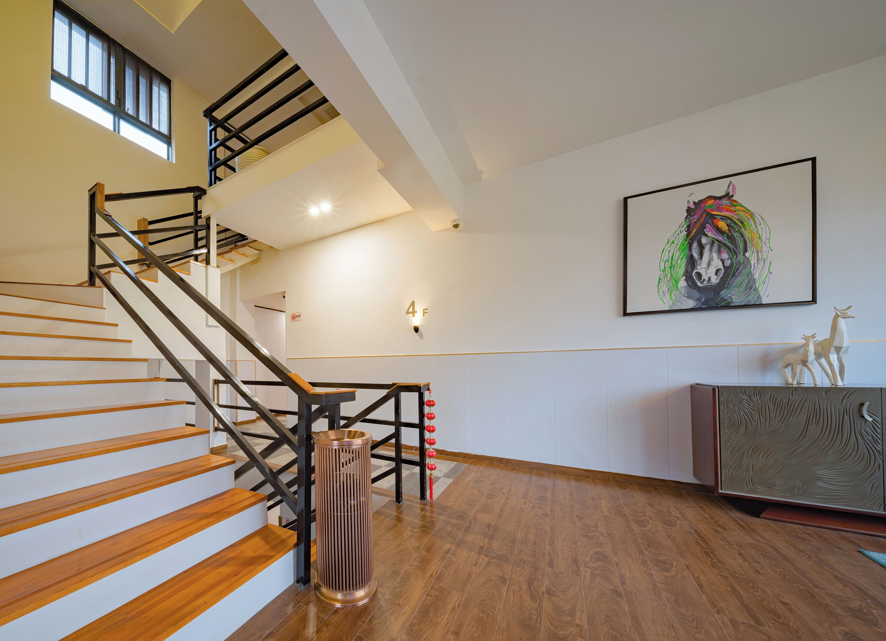 A modern interior with a wooden staircase, a metal railing, a wall-mounted light fixture, and a framed artwork.