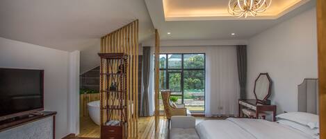 A modern hotel room with a large bed, a TV, a wooden bookshelf, a desk, and a view of the outdoors.