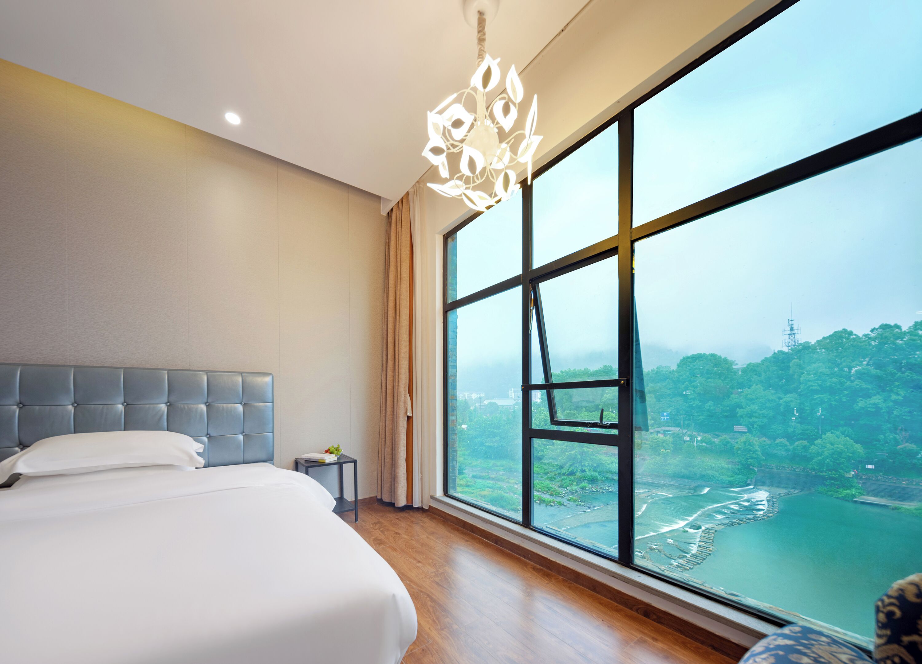 Une chambre d’hôtel moderne dotée d’un grand lit, offrant une vue sur une rivière et la verdure, et agrémentée d’un lustre unique.