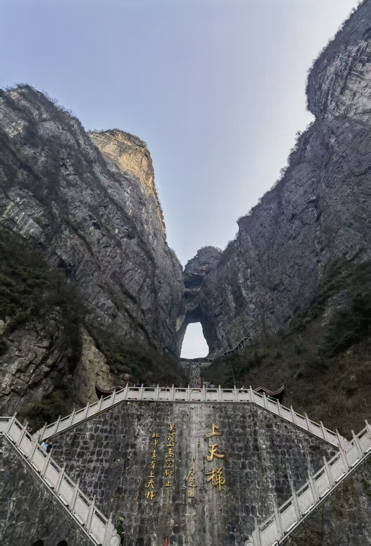 A stone bridge with Chinese characters, leading to a natural rock formation.