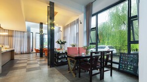 A modern hotel lobby with a checkered floor, a reception desk, a dining area with a table and chairs, and large windows offering a view of the outdoors.