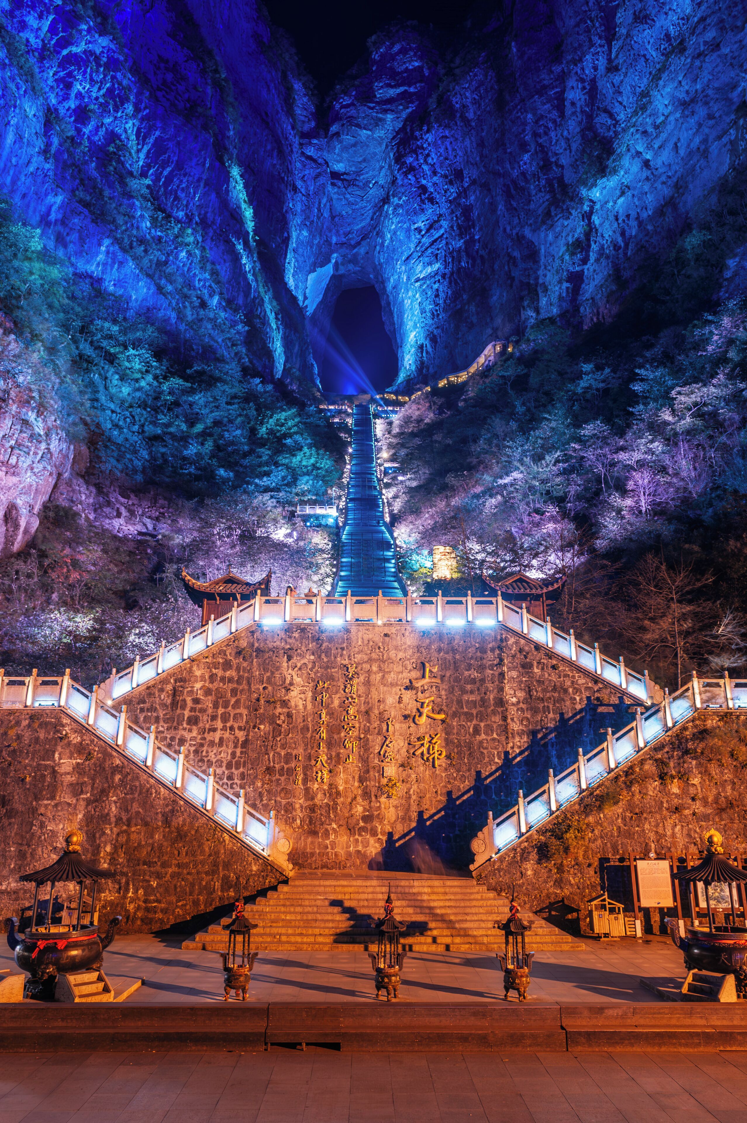 A stone staircase leading up to a temple with traditional Chinese architecture, surrounded by trees and illuminated by blue lighting.