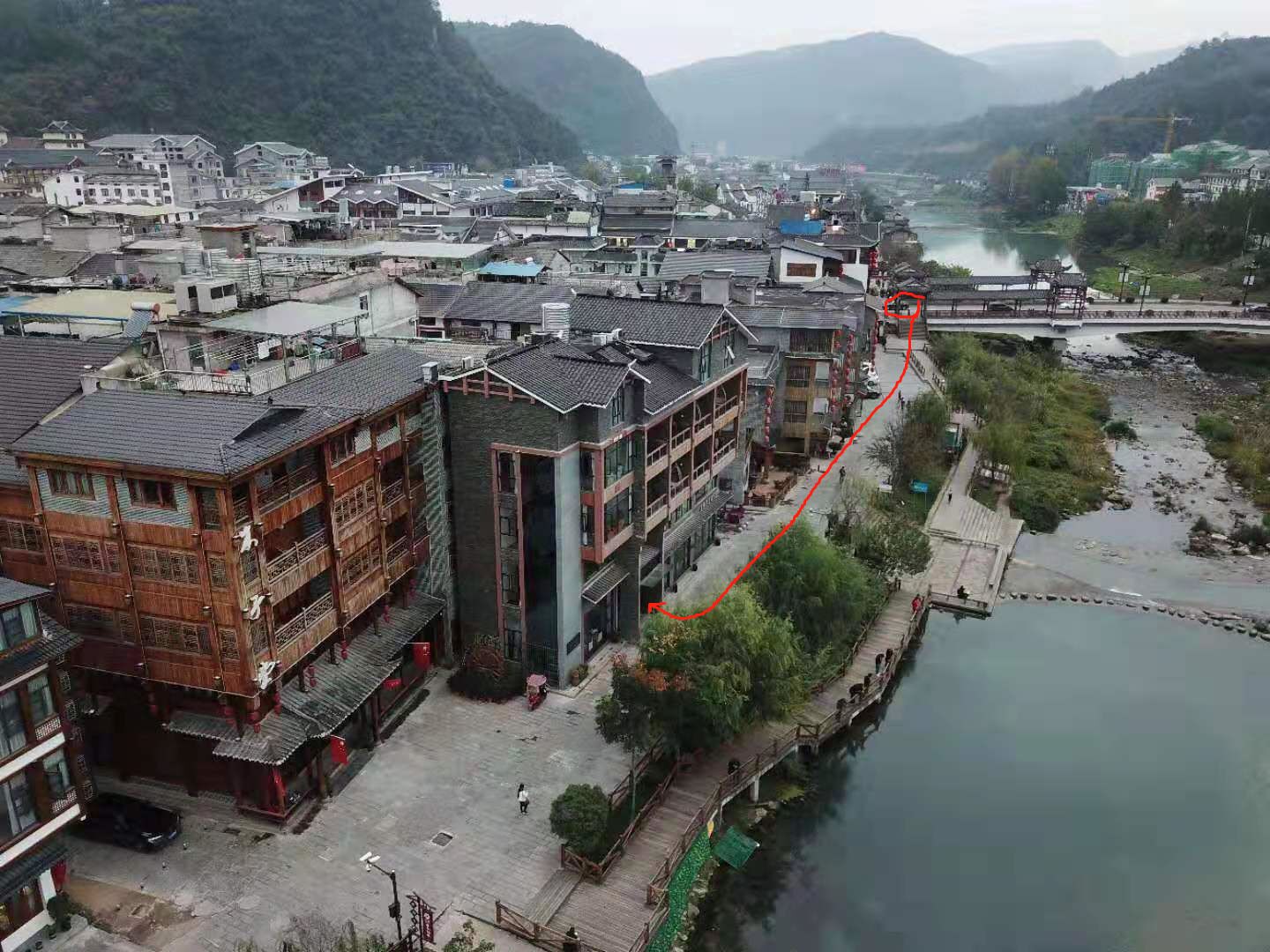 A riverside town with traditional and modern buildings, a wooden bridge, and a calm river.