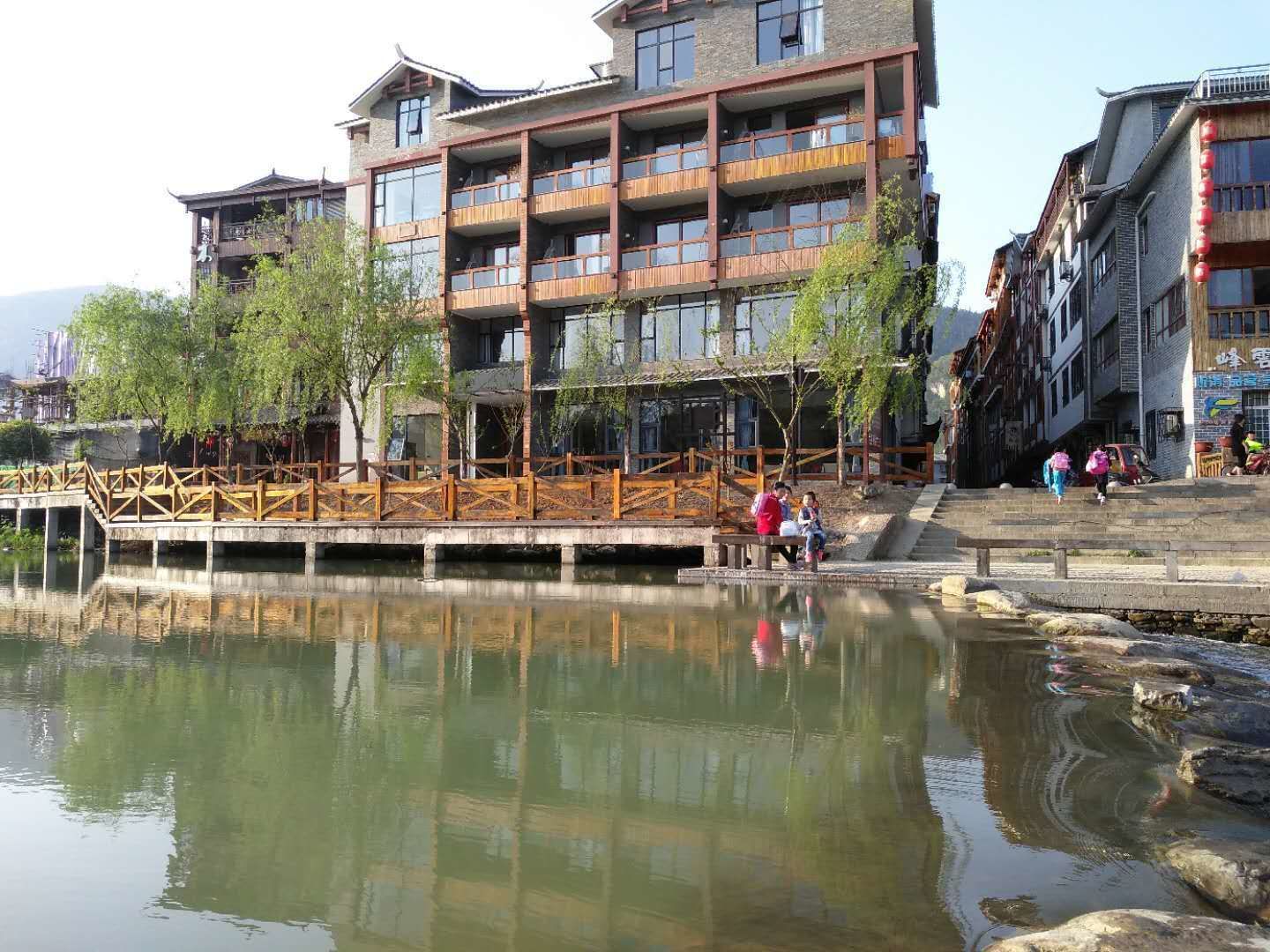 A multi-story building with balconies, a wooden bridge over a body of water, and a stone staircase leading to the entrance.