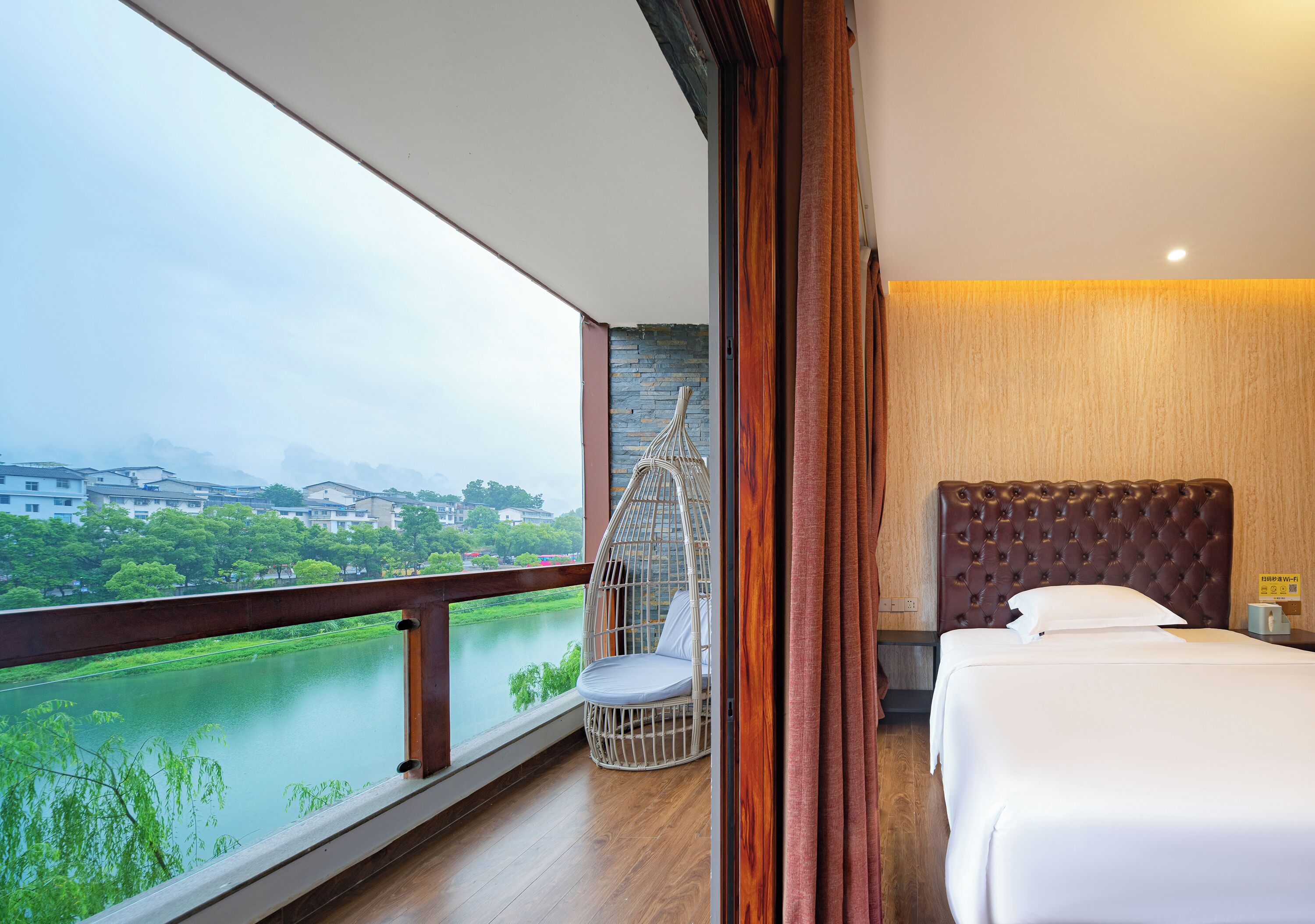 Habitación de hotel con balcón, cama, sillón colgante y vista al río.