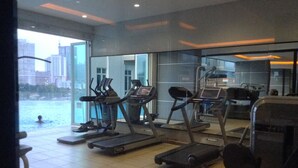 A gym with treadmills and exercise equipment, large windows overlooking a body of water and cityscape. - HomeStay in Johor - KSL SeaView (Johor Bahru)