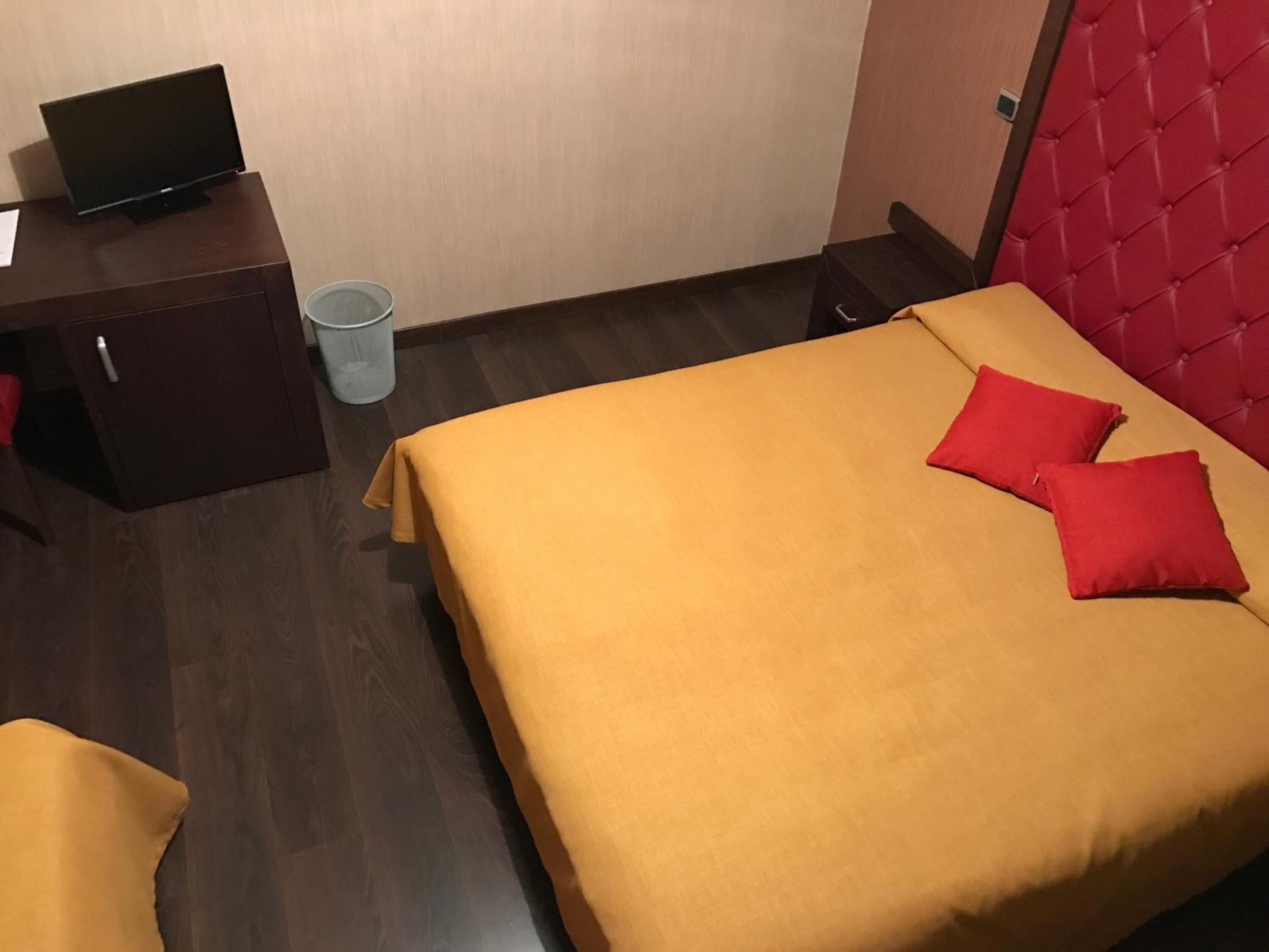 A hotel room with a bed, a desk with a computer, and a trash bin.