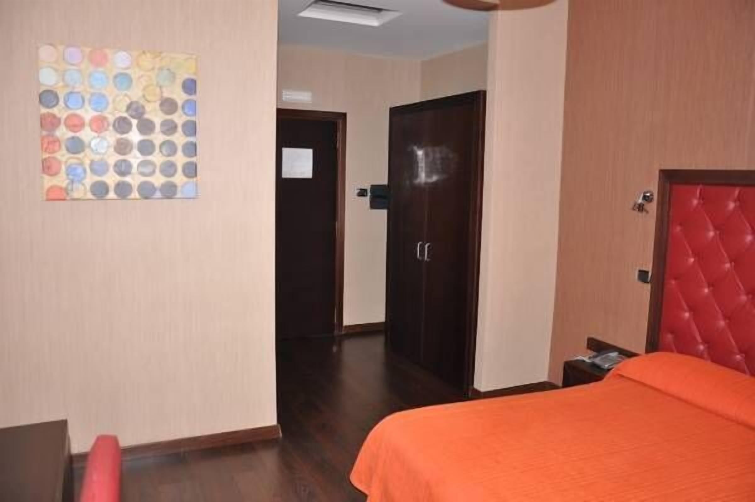 A hotel room with a bed, a red headboard, a wooden door, and a wall with a circular pattern.