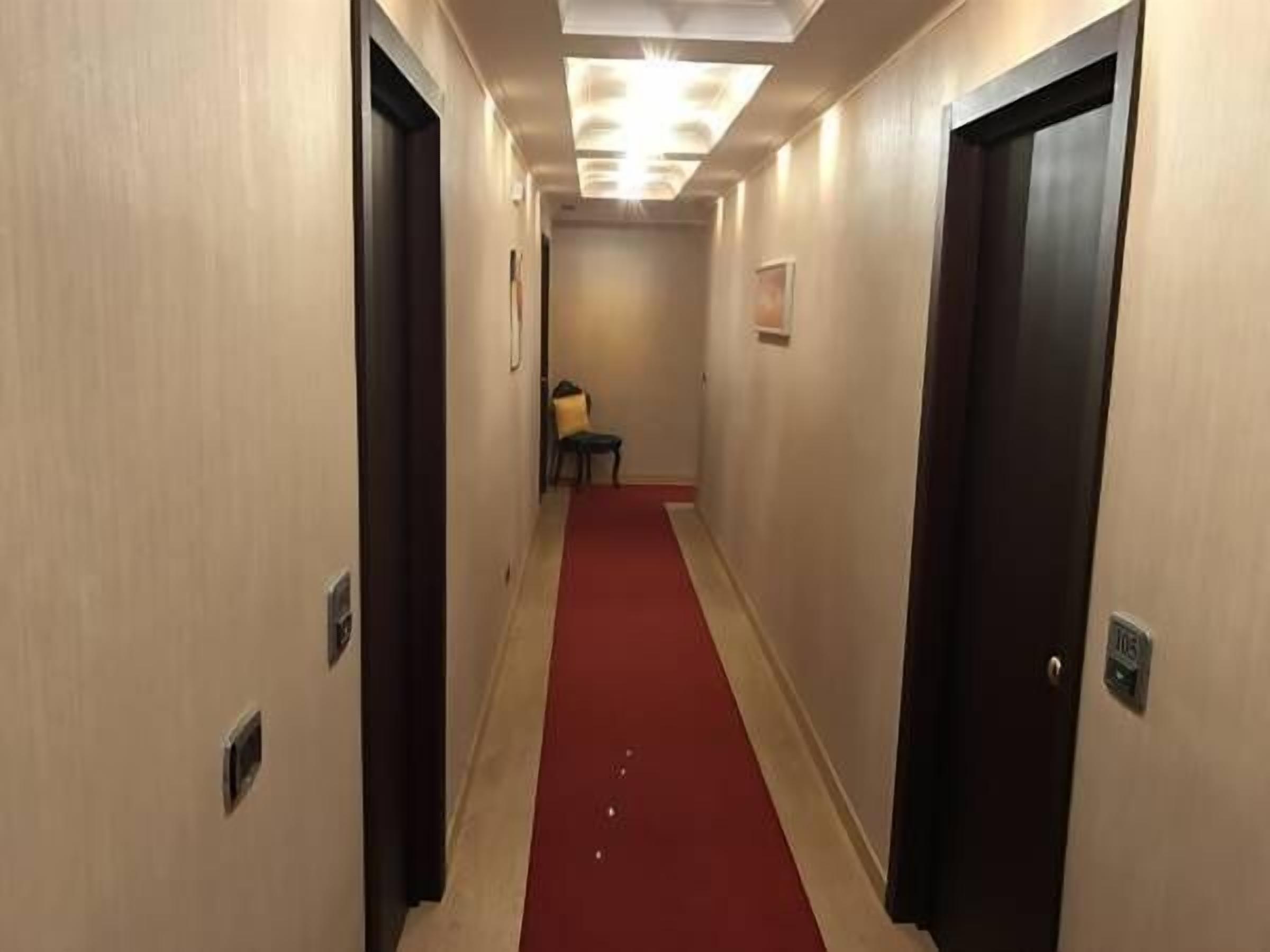 Un couloir d’hôtel avec un tapis rouge, des portes en bois et un luminaire au plafond.