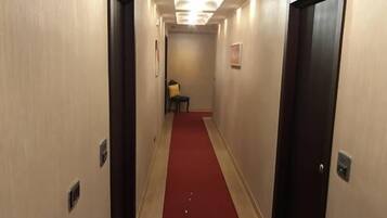 Un couloir d’hôtel avec un tapis rouge, des portes en bois et un luminaire au plafond.