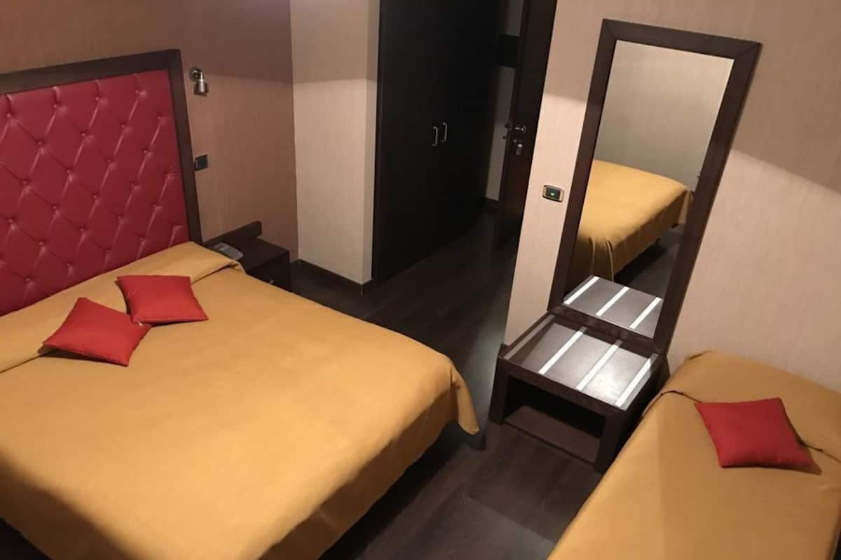 Ett hotellrum med två sängar, var och en med en röd sänggavel och gult sänglinne. Mellan sängarna står ett litet bord och på väggen hänger en spegel.