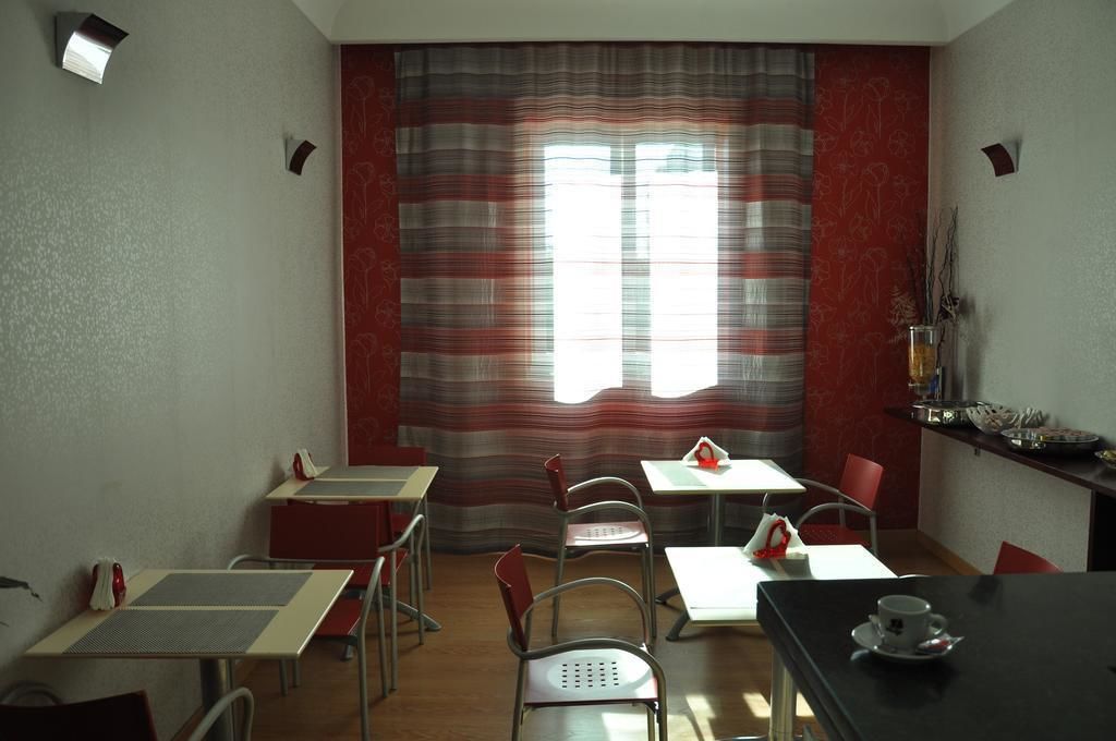 Un'area pranzo con tavoli e sedie, una finestra con tende e una mensola a muro con oggetti.