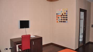 Habitación de hotel con escritorio, una silla roja, televisor montado en la pared y una obra de arte colorida.