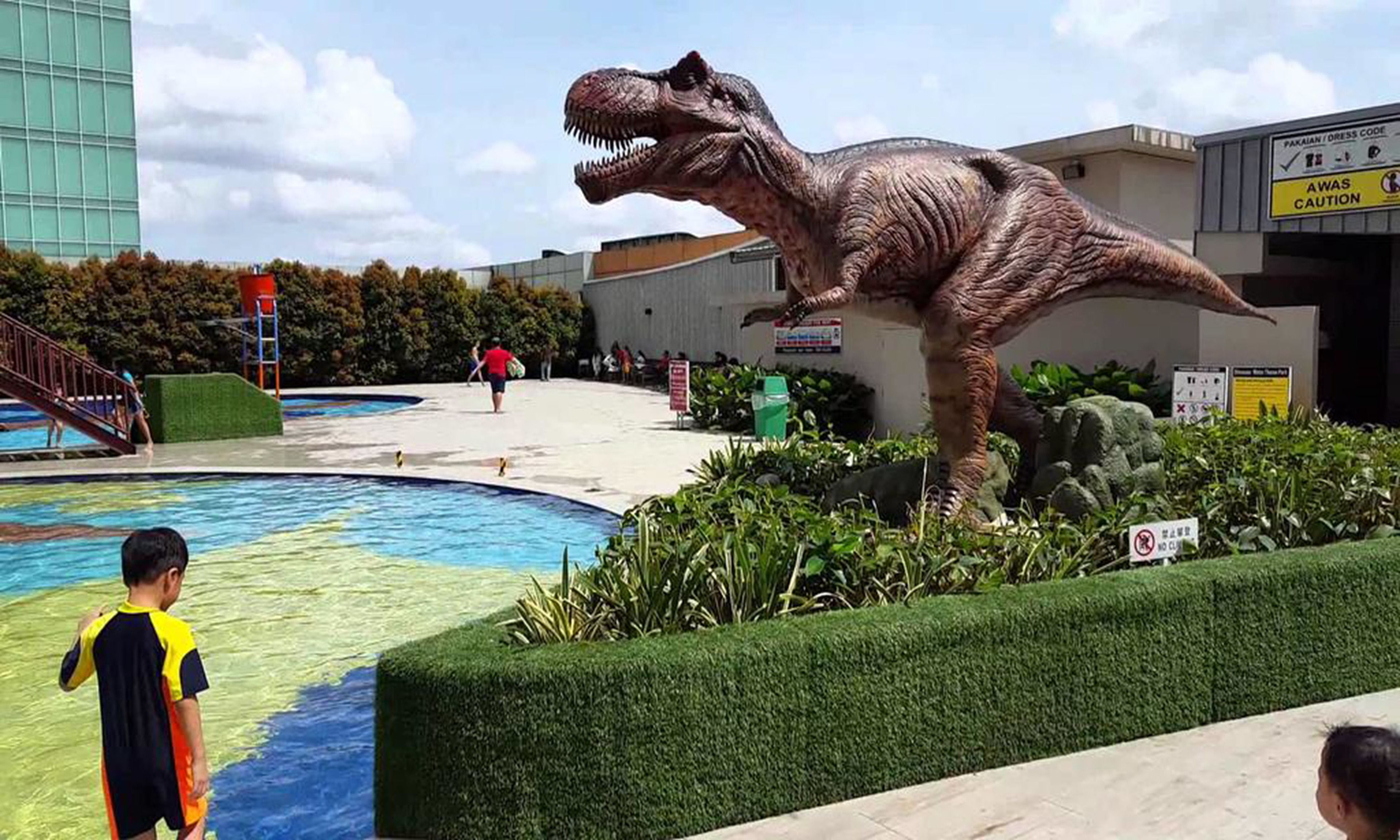 A dinosaur statue near a swimming pool with a building in the background.