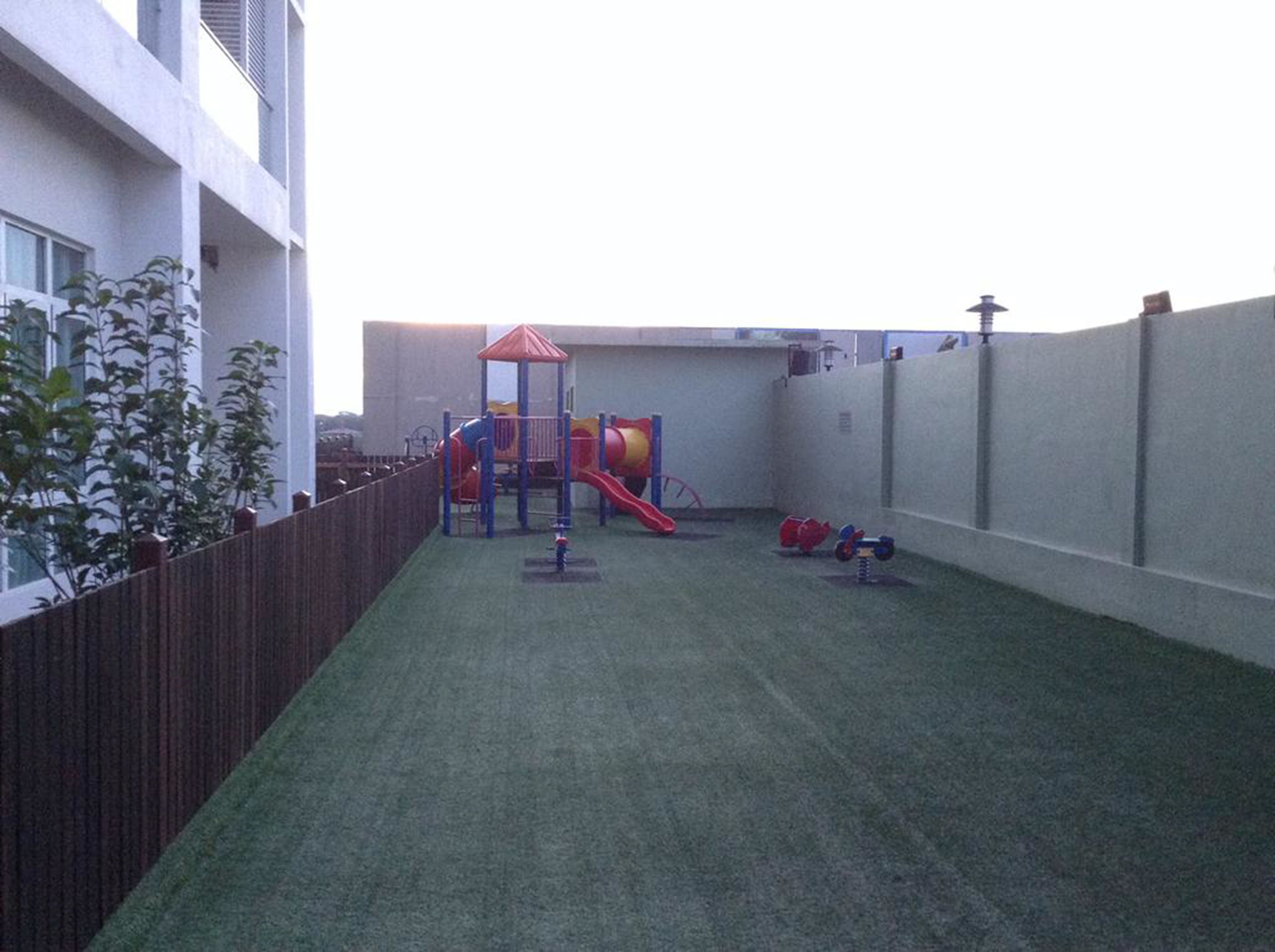 Cortile recintato con erba sintetica, un'area giochi per bambini e un piccolo giardino con piante.