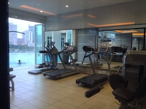 A gym with treadmills and exercise equipment, large windows overlooking a body of water and cityscape. - HomeStay D'Esplanade - Sweet Home (Johor Bahru)