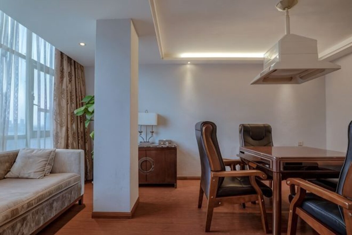 A modern room with a sofa, dining table, chairs, a lamp, and a large window with curtains.